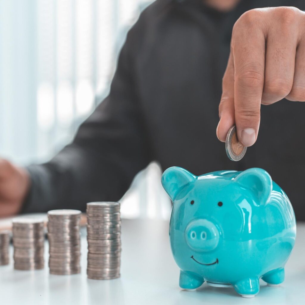 Geschäftsperson legt Münzen neben ein Sparschwein – symbolisiert Kosteneinsparung für Gewerbekunden